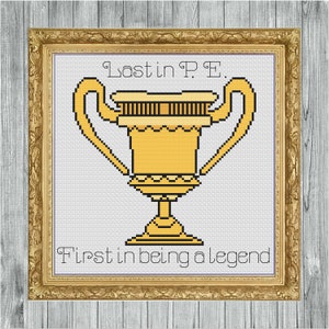 Puede incluir: Obra de arte de punto de cruz en un marco dorado. La imagen muestra un trofeo dorado pixelado con el texto "Last in P.E." arriba y "First in being a legend" abajo. El fondo es blanco.