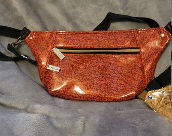 May include: A small orange fanny pack with a black strap and a gold zipper. The bag has a black and white pattern and a shiny finish.