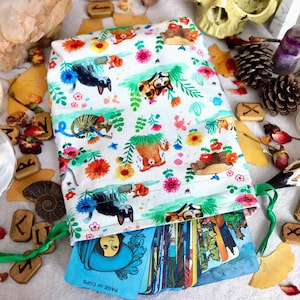 May include: A white tarot card bag with a colourful pattern of animals and flowers, filled with tarot cards. The scene includes candles, crystals, runes, and a skull, creating a mystical aesthetic.