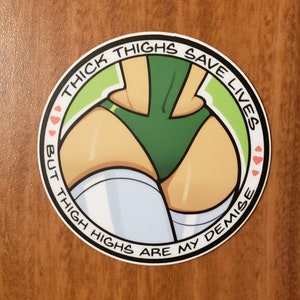 May include: A round sticker featuring an illustration of a person's lower body in a green swimsuit and white thigh-high socks. The sticker has the text "THICK THIGHS SAVE LIVES BUT THIGH HIGHS ARE MY DEMISE" in a circular design.