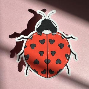 May include: A red ladybug sticker with black hearts on its back. The ladybug has black eyes and antennae.