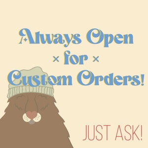 May include: A cartoon illustration of a brown bear wearing a gray knit hat with the text "Always Open for Custom Orders! JUST ASK!" in blue and yellow letters.