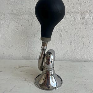 Puede incluir: Un claxon de bicicleta vintage con una pera de goma negra y una bocina de metal cromado brillante. La bocina tiene un diseño curvo y una base acampanada. Diseñado para ser montado en una bicicleta.