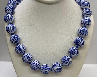 May include: A white and blue porcelain necklace with round beads featuring a repeating Chinese knot design. The necklace is on a white mannequin.