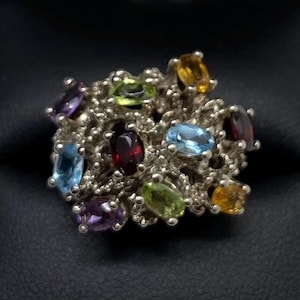 Può includere: Un anello d'argento con un gruppo di pietre preziose colorate, tra cui ametista, granato, peridoto, topazio e acquamarina.