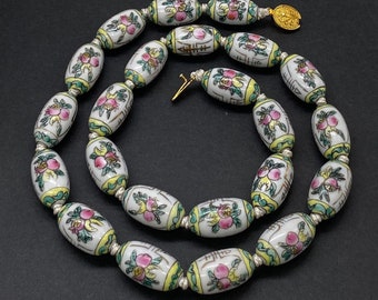 May include: A white porcelain necklace with oval beads featuring floral and Chinese character designs in pink, green, and gold. The necklace has a gold clasp.