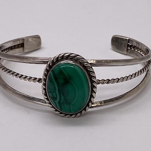 May include: Silver cuff bracelet with a large oval malachite stone. The green stone is set in a silver frame with a twisted rope design. Two additional silver bands with a twisted rope design are also present.