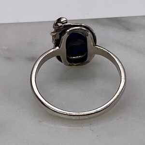 May include: A silver ring with a blue gemstone set in a decorative swirl design.
