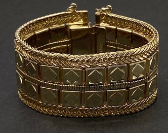May include: A gold bracelet with a textured design. The bracelet is made of multiple linked squares with a braided edge.