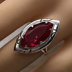 May include: A silver ring with a large, faceted, red gemstone set in a detailed, ornate design.