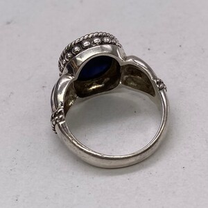Peut inclure: Une bague en argent avec une pierre pr&eacute;cieuse bleue sertie dans un sertissage &agrave; b&eacute;li&egrave;re. La bague a une bande d&eacute;corative avec un motif en forme de corde.