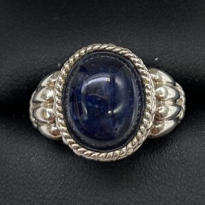 Peut inclure: Une bague en argent avec une pierre ovale bleu fonc&eacute; sertie dans une bordure en forme de corde. La bande de la bague a un design textur&eacute;.
