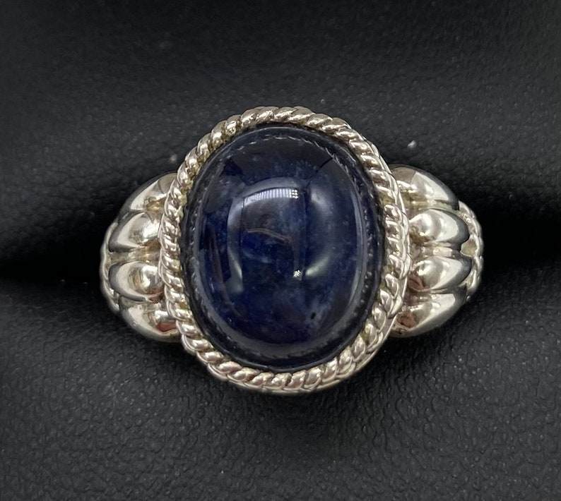 Peut inclure: Une bague en argent avec une pierre ovale bleu fonc&eacute; sertie dans une bordure en forme de corde. La bande de la bague a un design textur&eacute;.