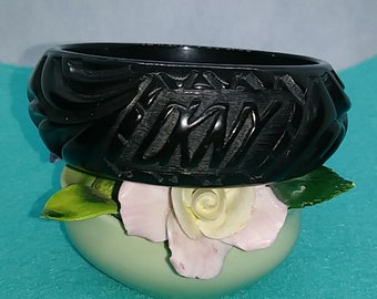May include: A black carved plastic bangle bracelet with a geometric design. The bracelet is thick and has a wide band.