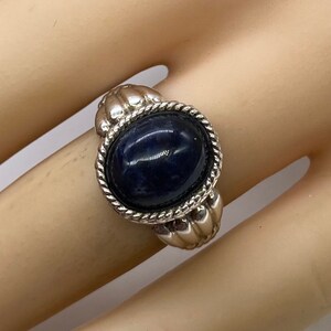 Peut inclure: Une bague en argent avec une pierre ovale bleu fonc&eacute; sertie dans une bordure en forme de corde. La bague a une bande textur&eacute;e.