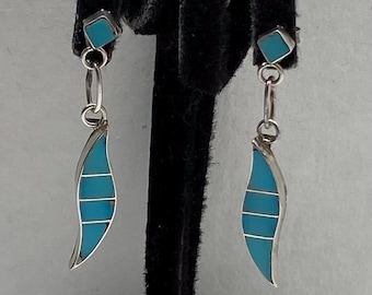 May include: Silver-toned dangle earrings with turquoise inlay. Each earring features a square stud, a chain, and a leaf-shaped pendant with three horizontal turquoise stripes. The earrings are displayed against a neutral background.