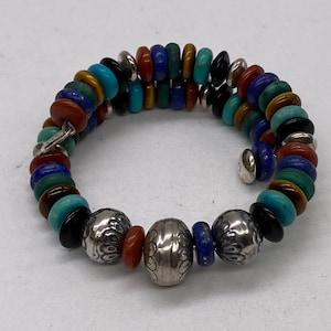 May include: A multi-coloured beaded bracelet with silver accents. The bracelet is made with turquoise, lapis lazuli, red, and green beads. The bracelet has two large silver beads with a textured design.