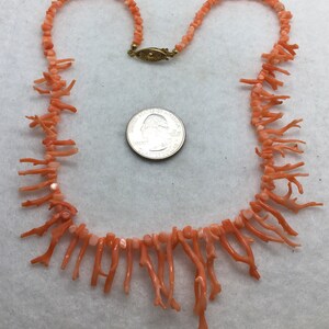 May include: A coral necklace with a gold clasp. The necklace is made of small, irregular coral pieces and has a fringe of longer coral branches.