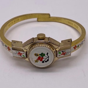 May include: Vintage gold-tone Swiss-made bracelet watch. The watch face is white with a floral design in red, green, and yellow. The bracelet has a floral pattern in red, green, and white. A unique piece of jewellery.