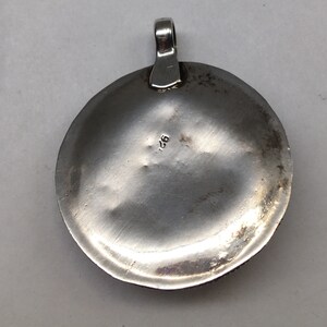 May include: Silver pendant with a round, slightly domed shape. The back of the pendant is smooth and has the number "925" stamped on it.