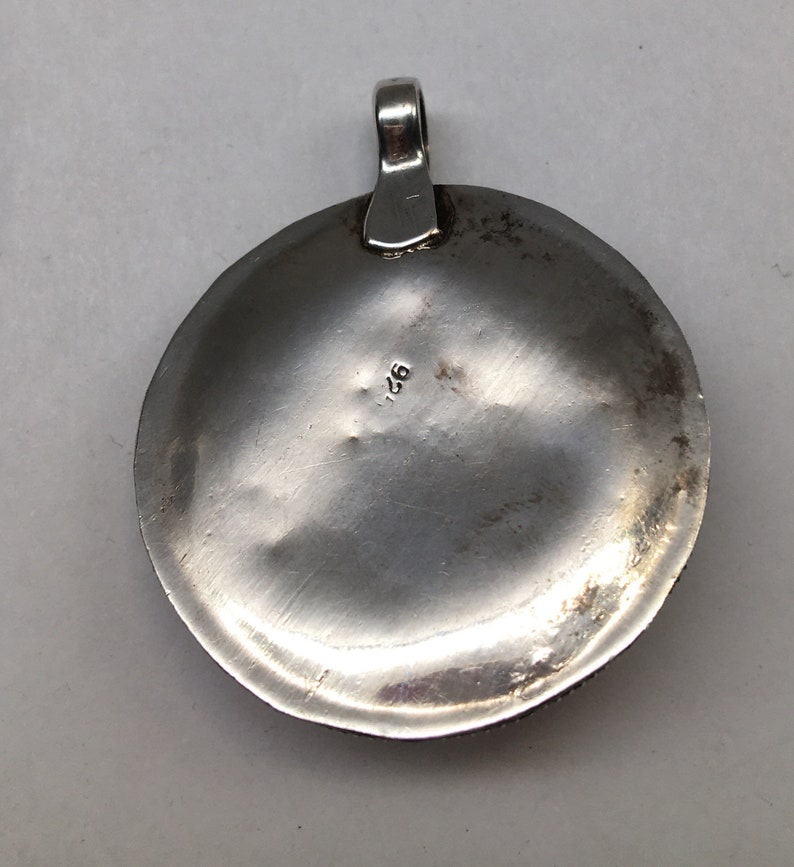 May include: Silver pendant with a round, slightly domed shape. The back of the pendant is smooth and has the number "925" stamped on it.
