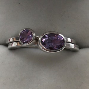 May include: Two silver rings with purple amethyst gemstones. The larger ring has an oval-shaped stone, while the smaller ring has a round stone.