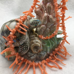 May include: A coral necklace made of small, irregular coral pieces and long, thin coral branches. The necklace is displayed on a ceramic turtle figurine.