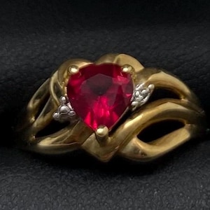 May include: A gold ring with a heart-shaped ruby gemstone and smaller diamonds on the band.