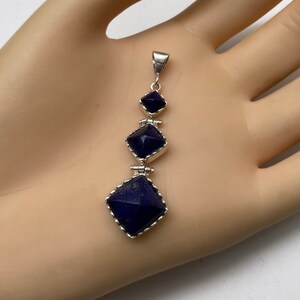 May include: A silver pendant with three square-shaped lapis lazuli stones. The stones are set in silver and have a faceted design. The pendant is approximately 2 inches long.