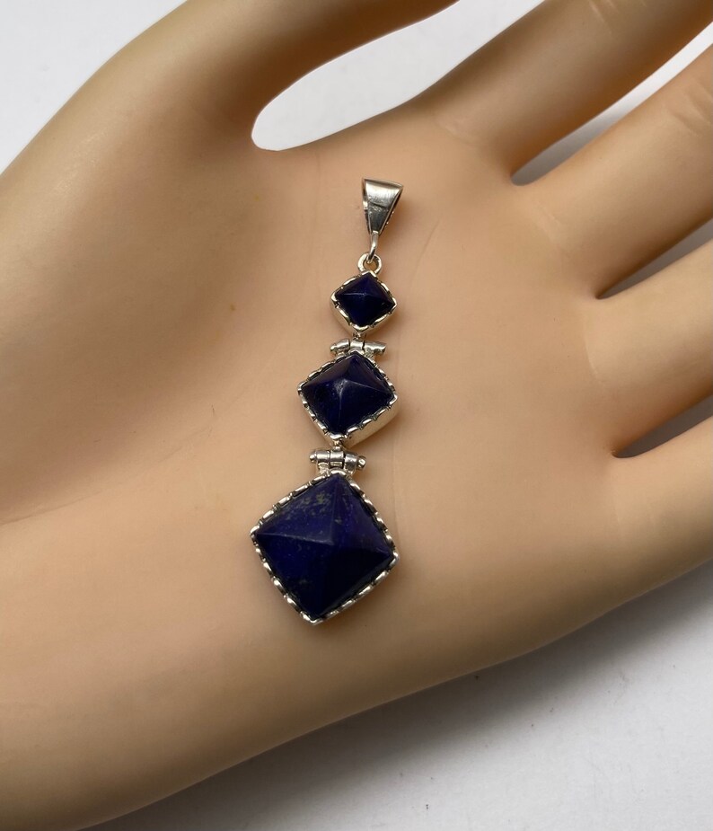 May include: A silver pendant with three square-shaped lapis lazuli stones. The stones are set in silver and have a faceted design. The pendant is approximately 2 inches long.