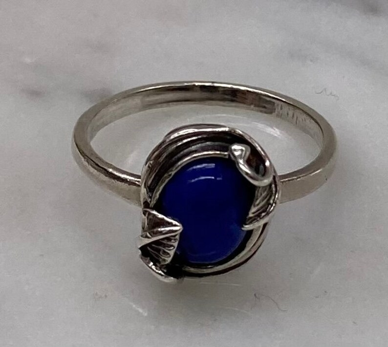 May include: A silver ring with a blue oval-shaped stone set in a delicate silver leaf design.