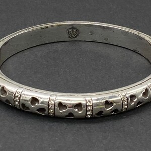 May include: Silver hinged bangle bracelet with a heart design and small clear stones.
