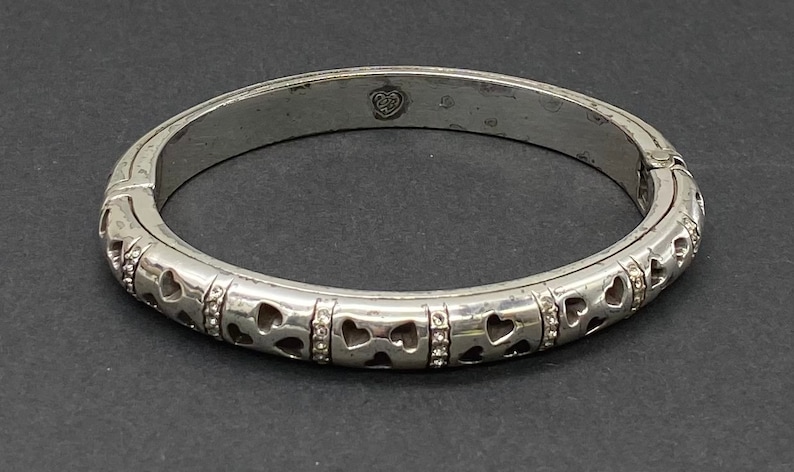 May include: Silver hinged bangle bracelet with a heart design and small clear stones.