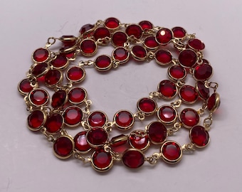 May include: A gold-toned necklace featuring numerous round, deep red gemstones. The gemstones are set in individual bezels and linked together with delicate gold chains. The necklace is displayed against a light background, highlighting the vibrant color of the stones.