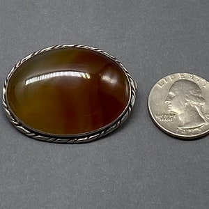 May include: A silver brooch with a brown agate stone set in a twisted wire frame. The brooch is about the size of a quarter.