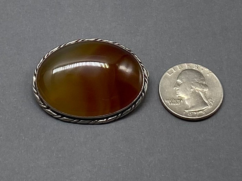 May include: A silver brooch with a brown agate stone set in a twisted wire frame. The brooch is about the size of a quarter.