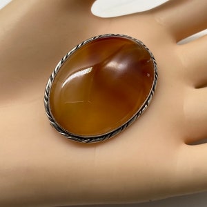 May include: A silver oval brooch with a large, smooth, orange carnelian stone set in a twisted wire frame.