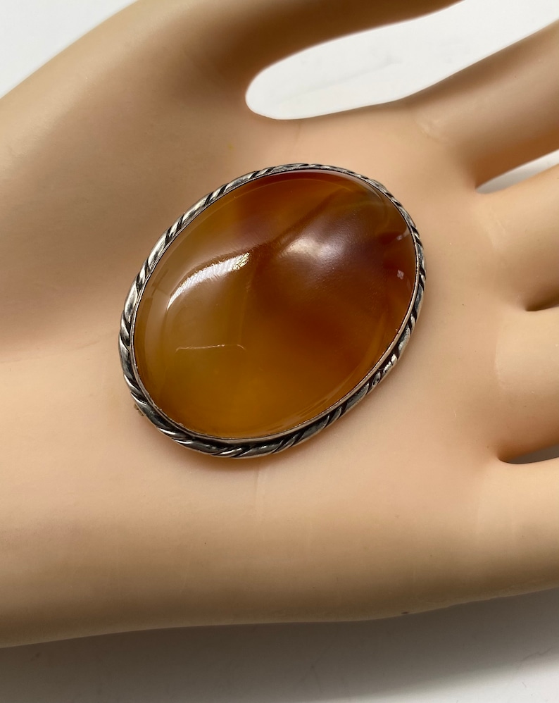 May include: A silver oval brooch with a large, smooth, orange carnelian stone set in a twisted wire frame.