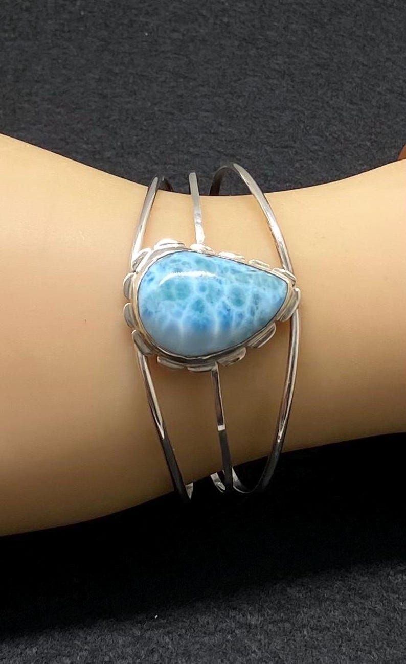May include: A silver bangle bracelet with a light blue gemstone set in the center. The gemstone has a unique marbled pattern.