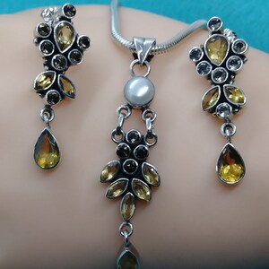 May include: A silver necklace and earrings set with a pearlescent pendant and multiple yellow and brown gemstones.