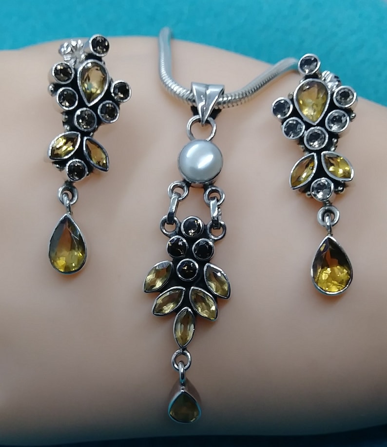 May include: A silver necklace and earrings set with a pearlescent pendant and multiple yellow and brown gemstones.