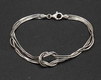 May include: A silver bracelet with a knotted design. The bracelet is made of multiple strands of chain.