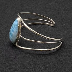 May include: A silver bracelet with a teardrop-shaped blue and white gemstone. The bracelet has a triple band design.