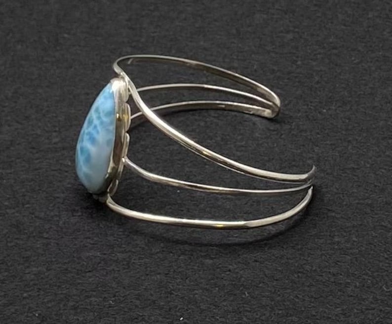 May include: A silver bracelet with a teardrop-shaped blue and white gemstone. The bracelet has a triple band design.