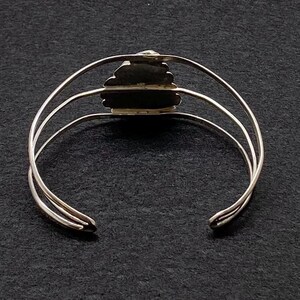 May include: Silver bangle bracelet with a decorative, textured, heart-shaped design.