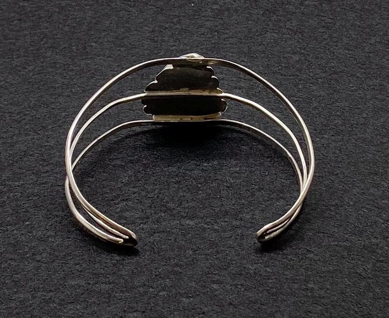 May include: Silver bangle bracelet with a decorative, textured, heart-shaped design.