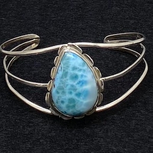 May include: A silver bracelet with a teardrop-shaped blue and white gemstone. The bracelet has a delicate, openwork design.