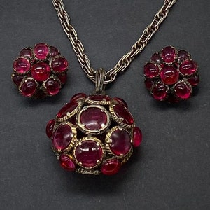 Op de afbeelding: Een zilveren ketting met een hanger en bijpassende oorbellen. De hanger en oorbellen zijn gemaakt van zilver en hebben een cluster van ronde, roze edelstenen.