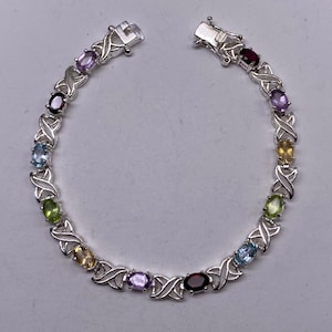 May include: A silver bracelet with a delicate, interwoven design features oval-shaped gemstones in a rainbow of colors, including amethyst, garnet, peridot, citrine, and aquamarine.