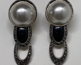 May include: A pair of silver earrings with a faux pearl drop and black accents. The earrings are decorated with marcasite stones.